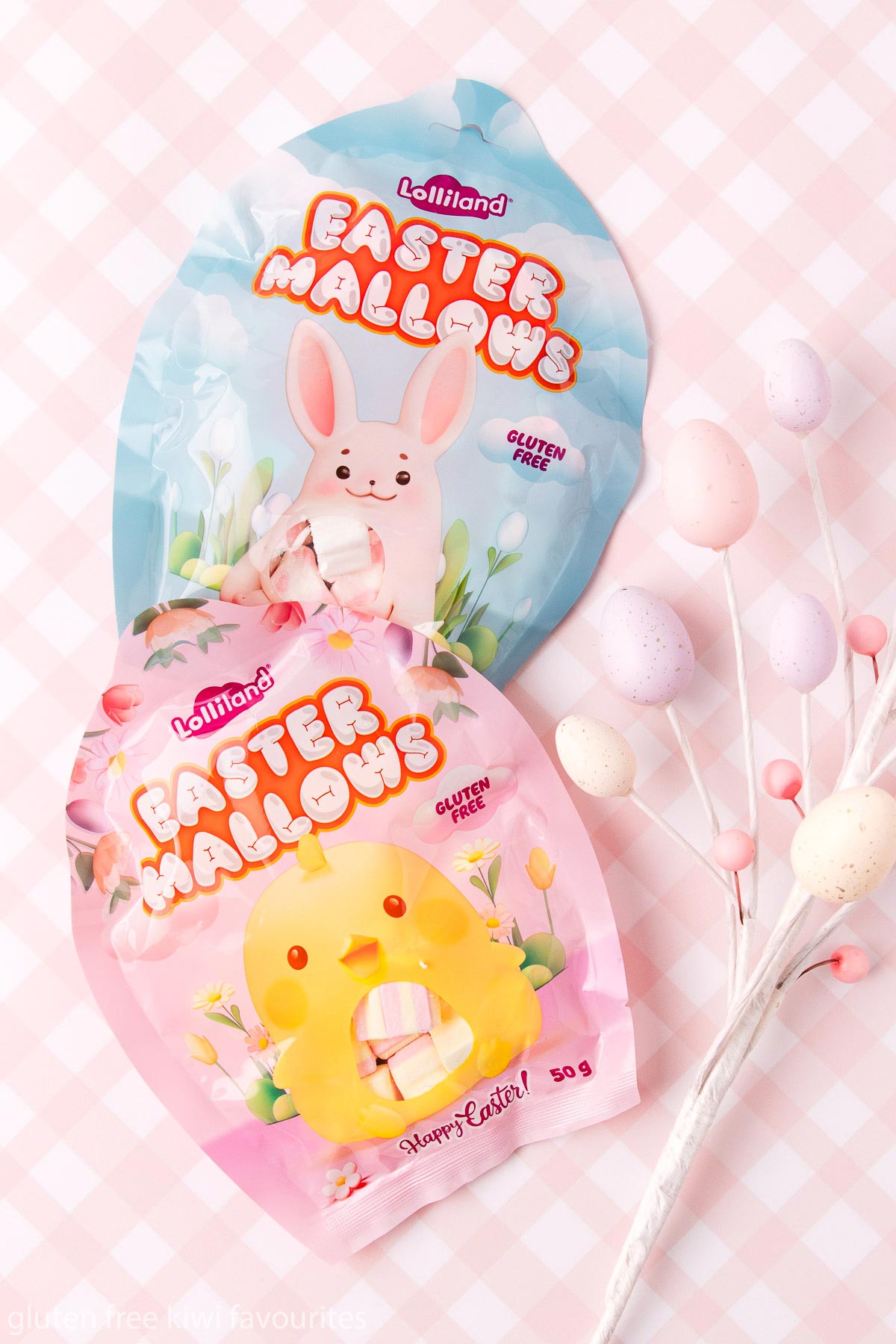 Two bags of Lolliland brand Easter Mallows, on a pink and white checked background.