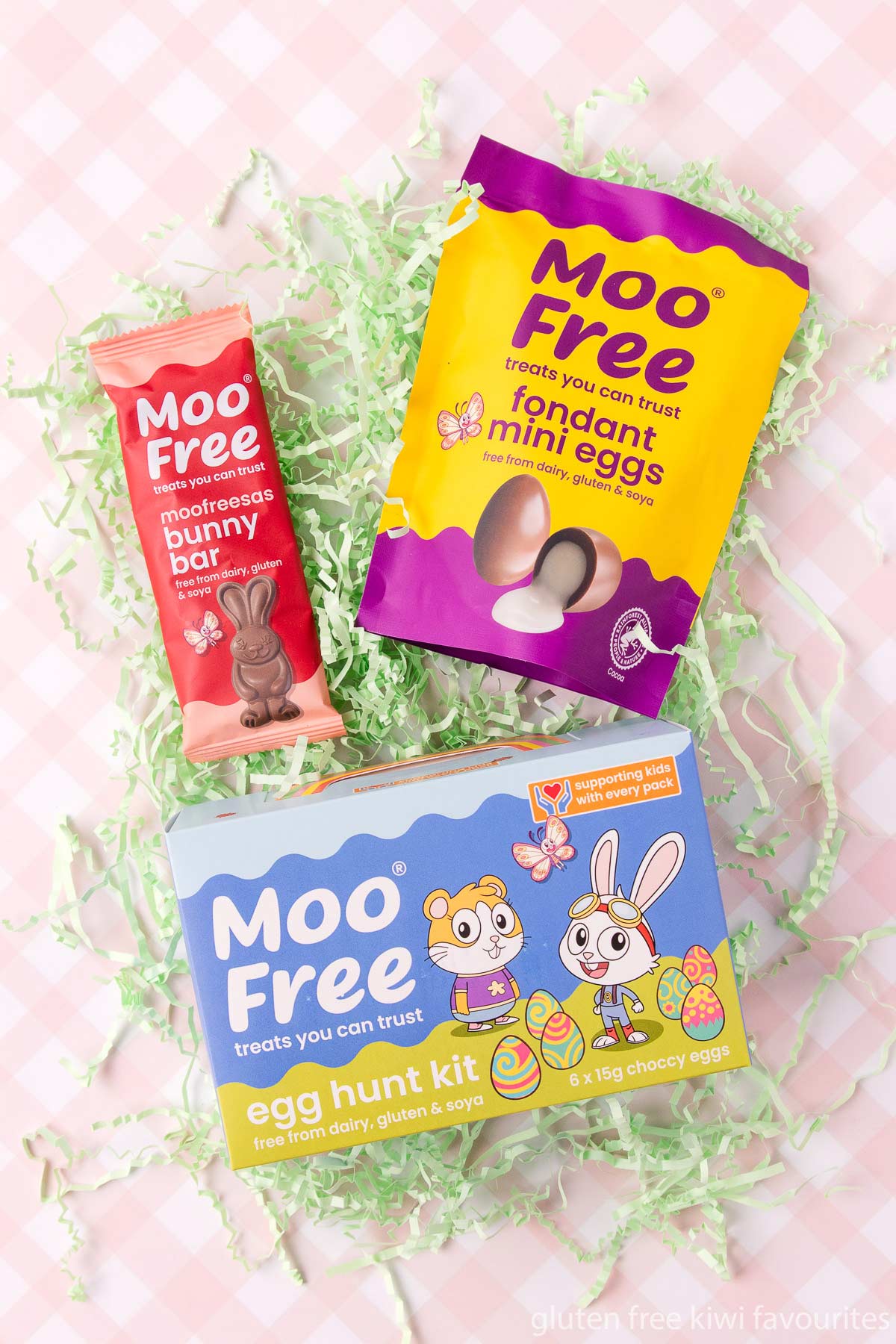 A bag of Moo Free fondant eggs, Easter hunt eggs and a small bunny bar, on a pink and white checked background.