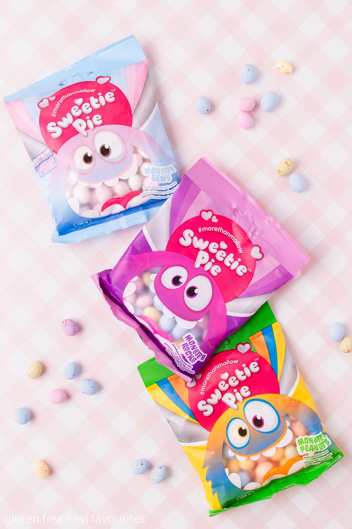 Three bags of Sweetie Pie brand Monster Gems, Monster Rocks and Monster Peanuts Easter eggs on a pink and white checked background.