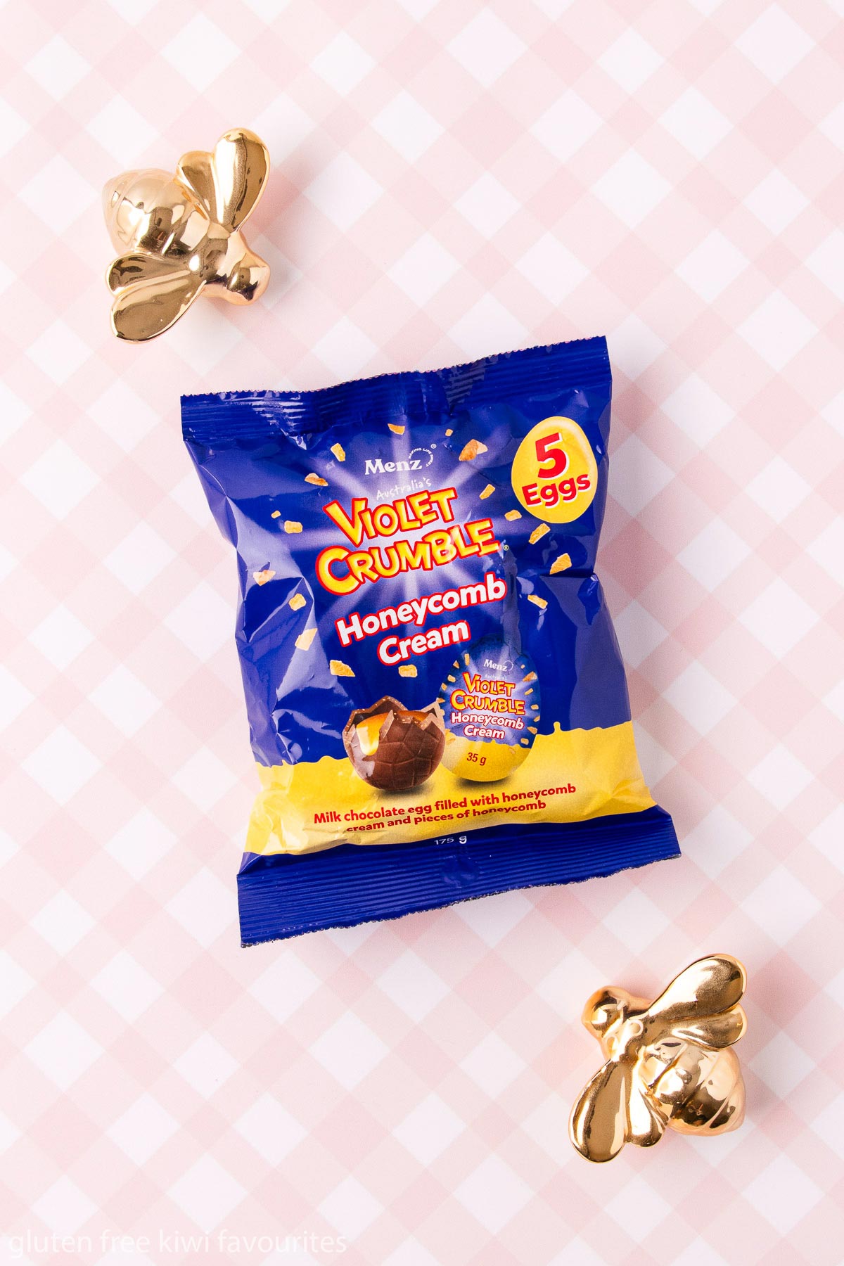 A bag of Violet Crumble honeycomb eggs on a pink and white checked background.